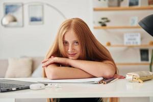 apoyado en la mesa. una adolescente con cabello rubio está en casa durante el día foto