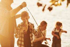 Illuminated by sunlight. Father and mother with son and daughter on fishing together outdoors at summertime photo