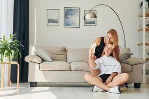 With phone in hands on the floor. Female teenager with her mother is at home at daytime photo