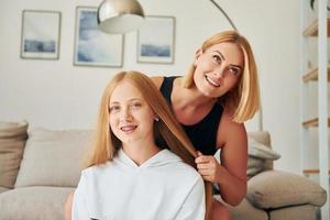 Parent helping with hair. Female teenager with her mother is at home at daytime photo