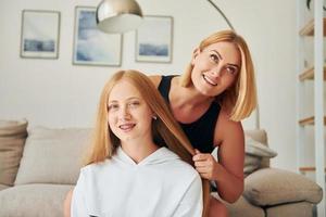 padre ayudando con el cabello. una adolescente con su madre está en casa durante el día foto