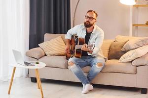 Cozy atmosphere. Man in casual clothes and with acoustic guitar is indoors photo
