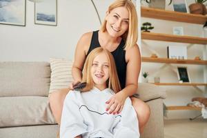 Parent helping with hair. Female teenager with her mother is at home at daytime photo