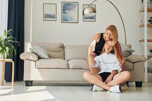 With phone in hands on the floor. Female teenager with her mother is at home at daytime photo