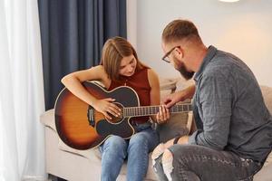 Private lesson. Guitar teacher showing how to play the instrument to young woman photo