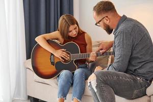 Private lesson. Guitar teacher showing how to play the instrument to young woman photo