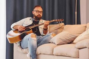 sentirse tranquilo. el hombre con ropa informal y con guitarra acústica está en el interior foto