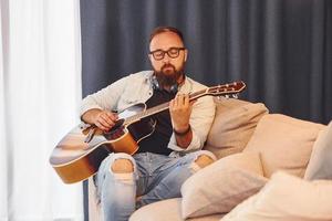 sentirse tranquilo. el hombre con ropa informal y con guitarra acústica está en el interior foto