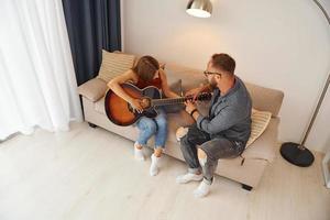 Private lesson. Guitar teacher showing how to play the instrument to young woman photo