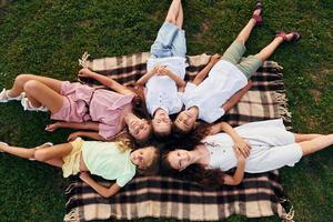 Having a rest and laying down. Group of happy kids is outdoors on the sportive field at daytime photo