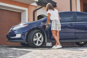 Car is on the electric charging station. Woman is outdoors with her modern automobile photo