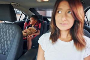 vista frontal. mujer con niño pequeño está en el automóvil moderno durante el día foto