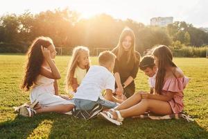 With woman. Group of happy kids is outdoors on the sportive field at daytime photo