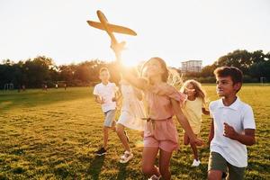 Playing with toy plane. Group of happy kids is outdoors on the sportive field at daytime photo