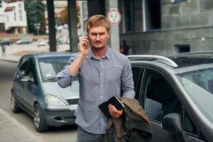 Talking by phone. Man having a walk outdoors in the city at daytime photo