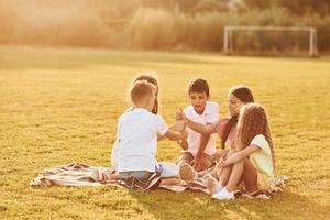 Beautiful sunlight. Group of happy kids is outdoors on the sportive field at daytime photo