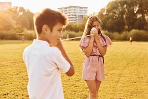 Kids having fun with tin can telephone. Standing outdoors on the sportive field photo