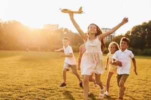 Playing with toy plane. Group of happy kids is outdoors on the sportive field at daytime photo