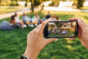 hacer fotos usando un teléfono inteligente. grupo de jóvenes tienen una fiesta en el parque durante el día de verano