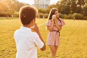 niños divirtiéndose con el teléfono de lata. de pie al aire libre en el campo deportivo foto