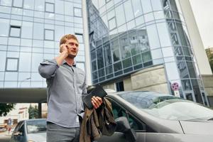 Talking by phone. Man having a walk outdoors in the city at daytime photo