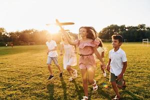 jugando con avión de juguete. grupo de niños felices está al aire libre en el campo deportivo durante el día foto