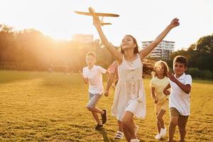 Playing with toy plane. Group of happy kids is outdoors on the sportive field at daytime photo