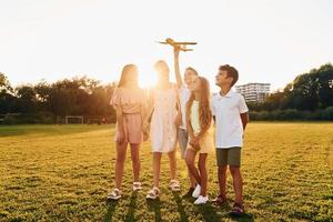 corriendo con avión de juguete. grupo de niños felices está al aire libre en el campo deportivo durante el día foto