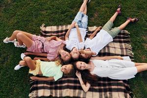 Having a rest and laying down. Group of happy kids is outdoors on the sportive field at daytime photo