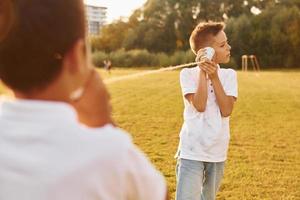 Two boys having fun by using tin can telephone on the sportive field photo