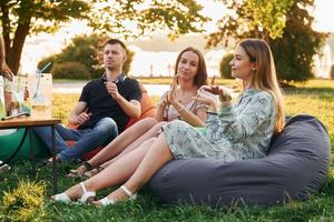 sentado cerca de la mesa con alcohol. grupo de jóvenes tienen una fiesta en el parque durante el día de verano foto