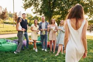 de pie con cócteles. grupo de jóvenes tienen una fiesta en el parque durante el día de verano foto