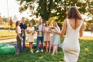 Standing with cocktails. Group of young people have a party in the park at summer daytime photo