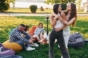 Women posing for the camera. Group of young people have a party in the park at summer daytime photo