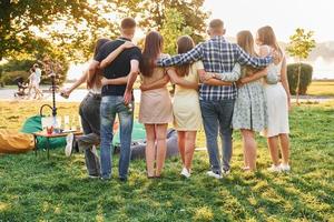 View from behind. Group of young people have a party in the park at summer daytime photo