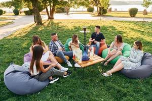 Sitting in the armchair bags and smoking hookah. Group of young people have a party in the park at summer daytime photo