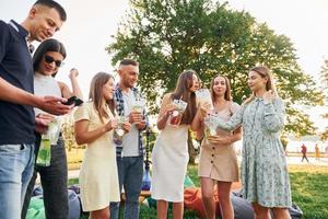 Having a drink. Group of young people have a party in the park at summer daytime photo