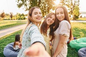 Female friends standing and having fun. Group of young people have a party in the park at summer daytime photo