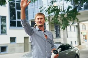 Hello gesture. Raises his hand up. Man having a walk outdoors in the city at daytime photo