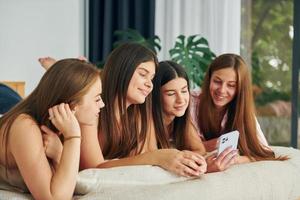 Laying down on bed with smartphone. Group of happy women that is at a bachelorette party photo