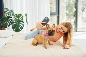 Doing selfie. Woman with pug dog is at home at daytime photo