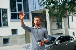 Hello gesture. Raises his hand up. Man having a walk outdoors in the city at daytime photo