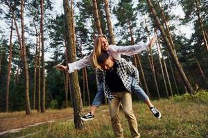 Woman is riding her man. Happy couple is outdoors in the forest at daytime photo