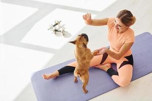 On fitness mat. Woman with pug dog is at home at daytime photo