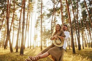 Man is in white shirt and woman in dress. Happy couple is outdoors in the forest at daytime photo