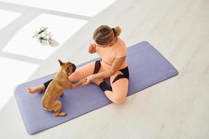 On fitness mat. Woman with pug dog is at home at daytime photo