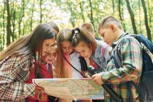 usando mapa. niños en el bosque verde durante el día de verano juntos foto