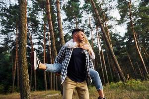 Woman is riding her man. Happy couple is outdoors in the forest at daytime photo