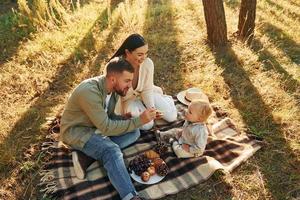 comiendo algo de comida. feliz familia de padre, madre e hija pequeña está en el bosque foto