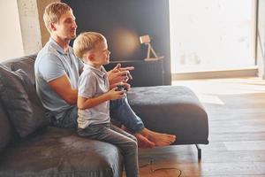 jugando videojuegos. padre e hijo están juntos en casa en el interior foto